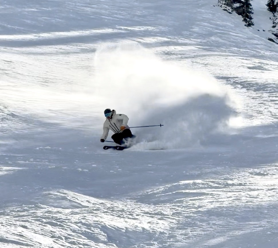 Oskar Lighthiser making a deep powder turn on a wide snowy slope, spraying snow behind him