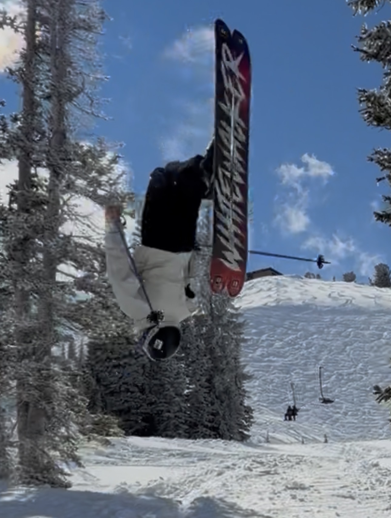Oskar Lighthiser inverted mid-air during a backflip on a bright blue-sky day, skis vertical above a snowy slope