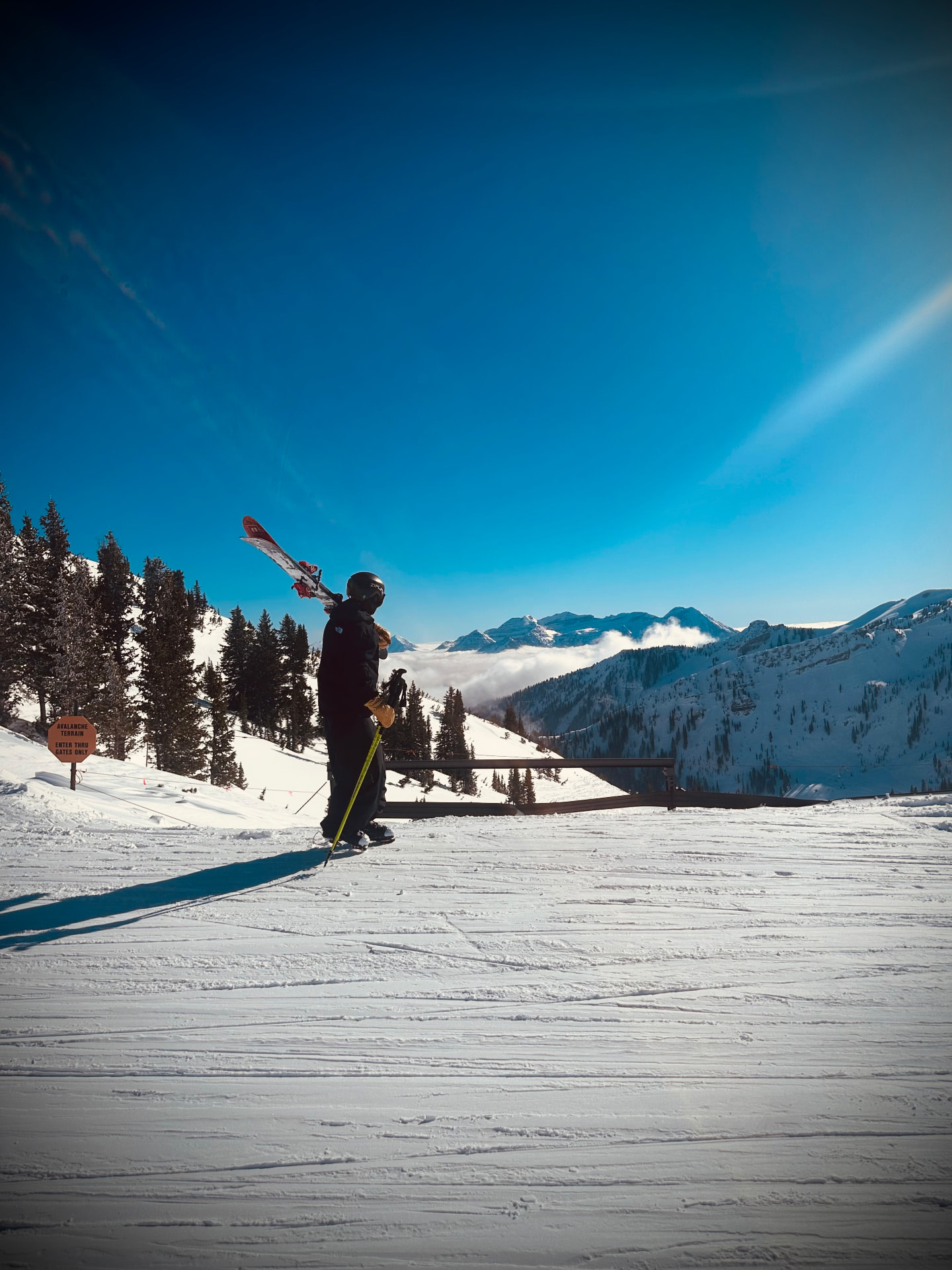 Oskar Lighthiser hiking with skis on his shoulder under a deep blue sky above a valley of clouds