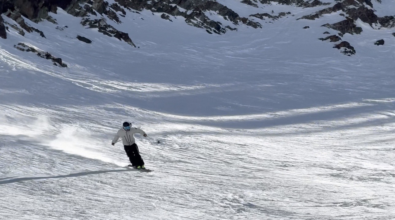 Oskar Lighthiser carving fast down a firm high-alpine slope with a spray of snow trailing behind